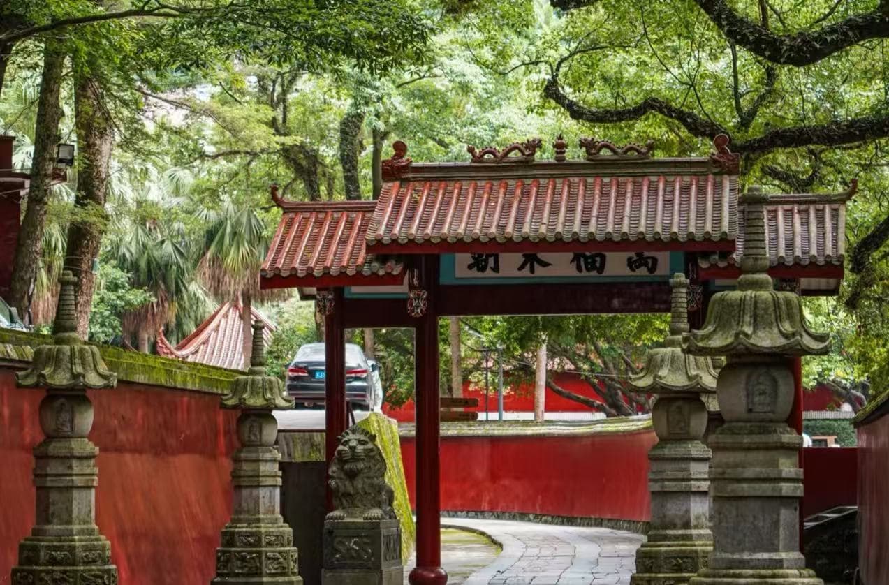 Yongquan Temple,Fuzhou,Chinatour Traditional Chinese temple gate with red tiled roof, stone lanterns, and a curved stone path surrounded by lush greenery.