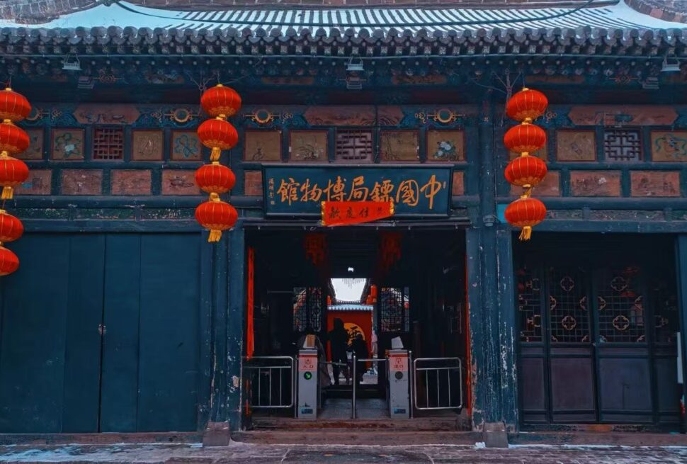 Traditional Chinese doorway decorated with red lanterns and gold Chinese signboard, teal walls, and carved panels above the entrance.