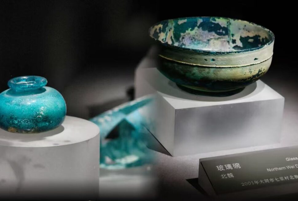 Blue-green ceramic bowls on white display plinths in a museum, with a label mentioning a glass bowl from the Northern Wei Dynasty and a date in Chinese characters.
