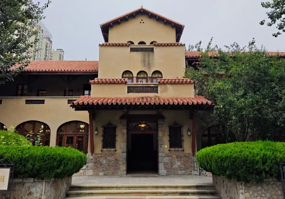Former Residence of Puyi Jingyuan Garden,Tianjin,Chinatour Villa-style building with red-tiled roof, arched windows, and a central entrance framed by trimmed hedges in a garden setting.