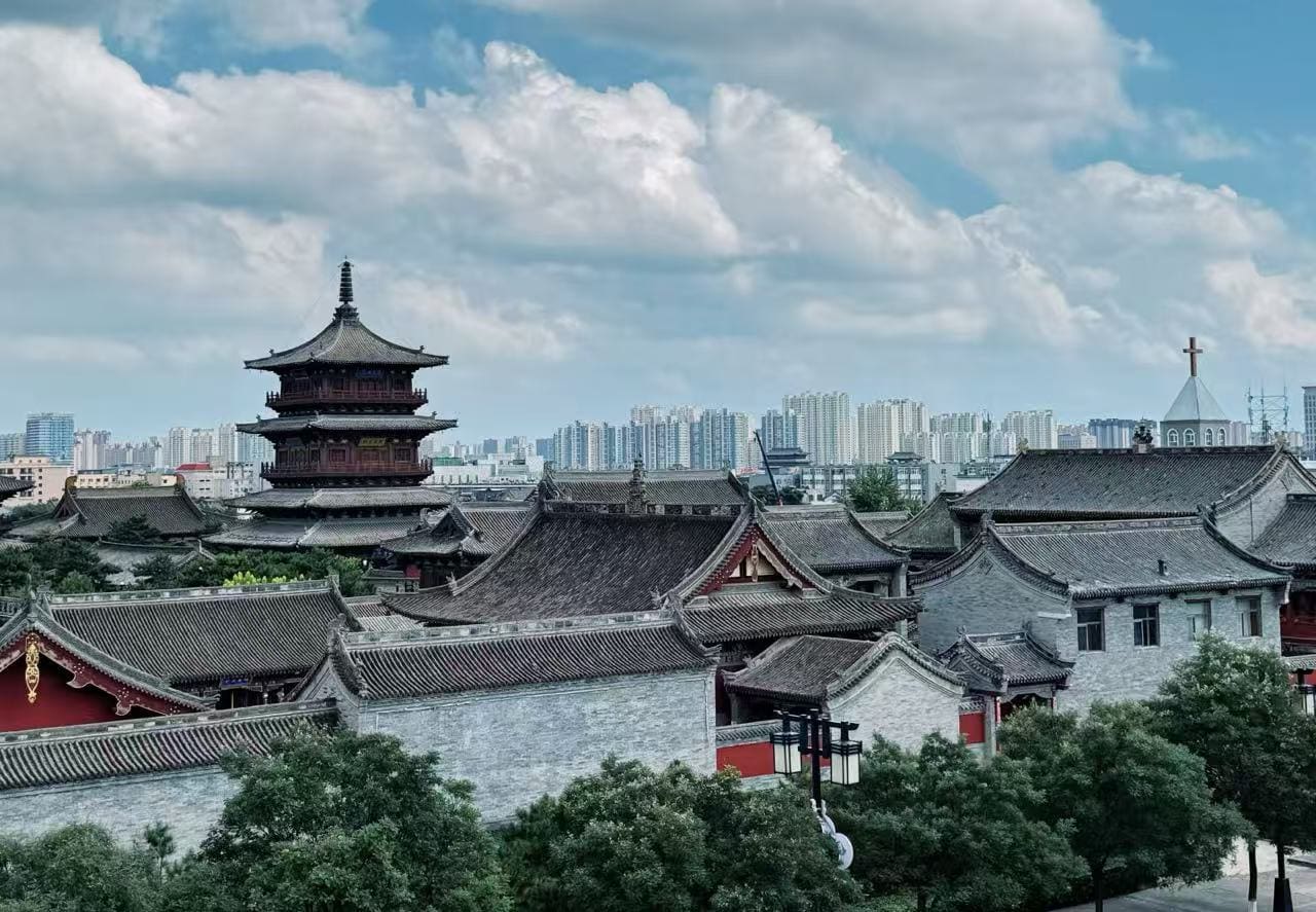Pingcheng Ancient Town,Datong,Chinatour Traditional Chinese temple complex with a multi-tier pagoda in the foreground and a modern city skyline in the distance under a blue sky.
