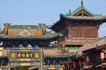 Ornate Chinese temple gate with colorful tiled roof, carved wood, and a decorative plaque in Chinese characters under a bright blue sky.