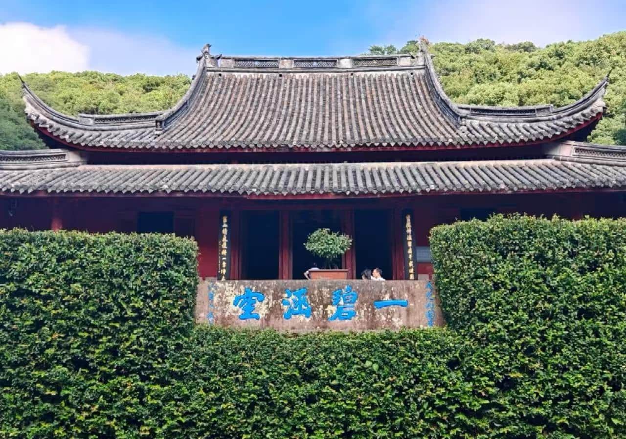 Baoguo Temple,Ningbo,Chinatour Traditional Chinese temple/pavilion with ornate tiled roofs and red walls, backed by greenery and a blue-character stone plaque in front.