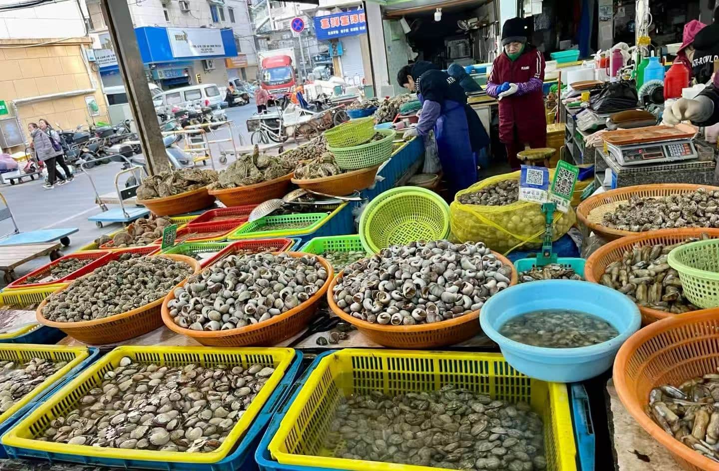 Donghe Market,Zhoushan,Chinatour Outdoor market seafood stall with baskets of clams and oysters on display, colorful tubs and crates in the foreground.