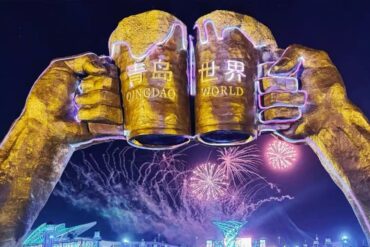 International Beer City,Qingdao,Chinatour Night view of giant golden fists forming an arch with the words 'QINGDAO WORLD' and colorful fireworks above a lit cityscape outside the venue.