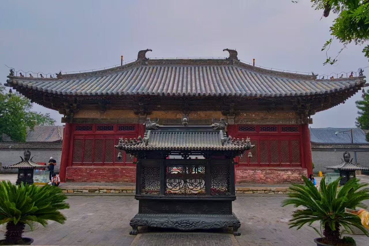 Traditional Chinese temple gate with a gray tiled roof and red wooden walls in a courtyard setting.