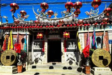 Front view of a Chinese temple entrance adorned with red lanterns, dragon sculptures, and decorative banners along the roof.