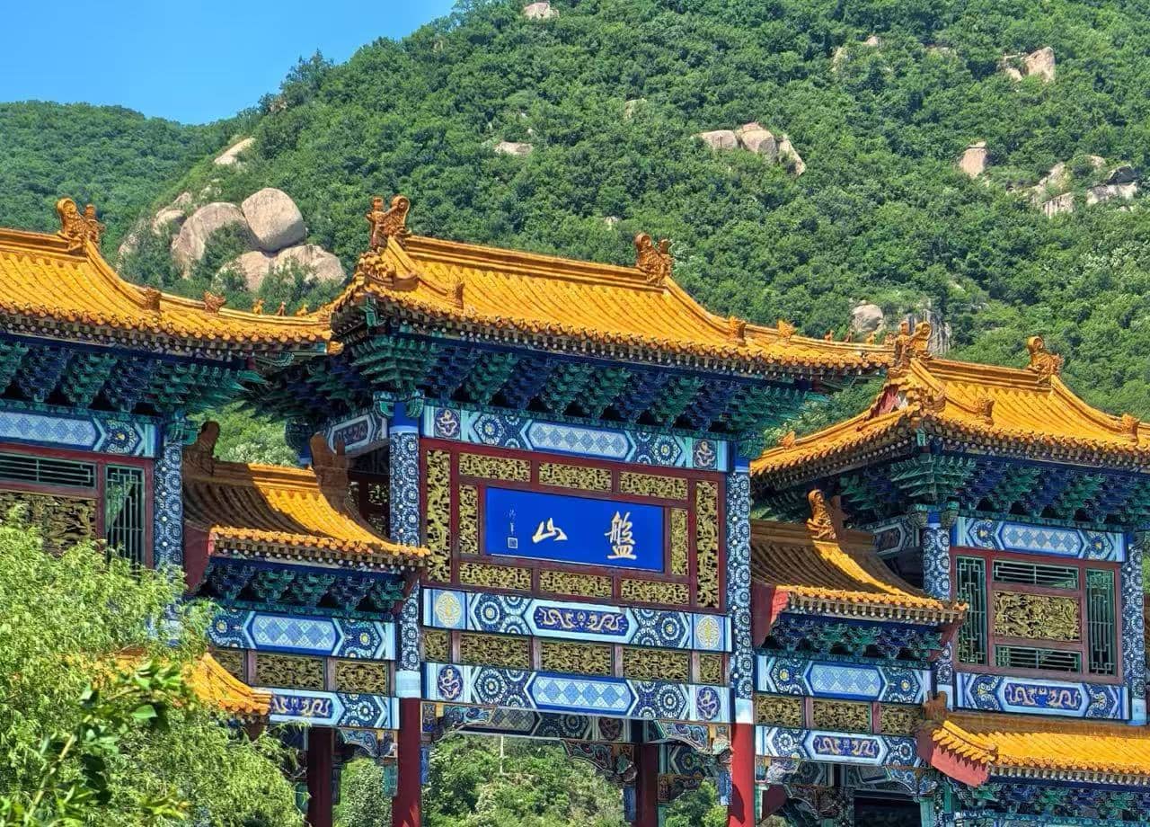 Panshan Mountai,Tianjin,Chinatour Ornate traditional Chinese gate with blue and gold decorative panels and orange tiled roofs, set against a green hillside mountain backdrop.