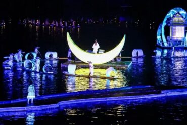 Nighttime water show with a glowing crescent moon float centerpiece and performers on floating platforms amid illuminated sculptures.Impression Sanjie Liu Show,Yangshuo,Guangxi,Chinatravel