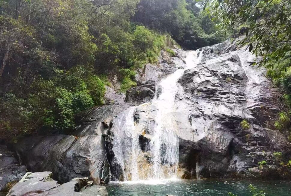 Huayan National Forest Park,Wenzhou,Chinatour Waterfall cascading down gray rocks into a tranquil pool, surrounded by dense green forest.