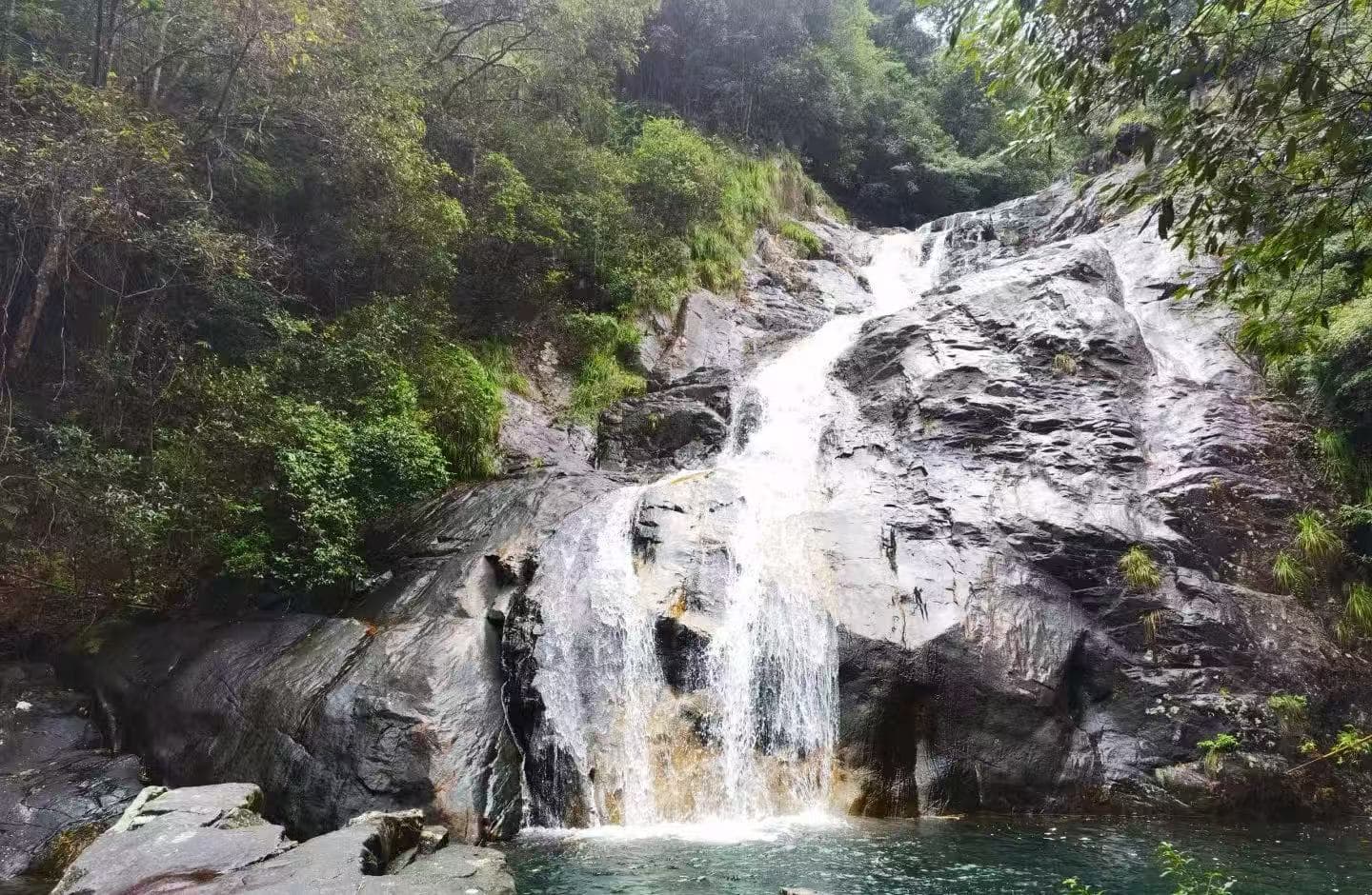 Huayan National Forest Park,Wenzhou,Chinatour Waterfall cascading down gray rocks into a tranquil pool, surrounded by dense green forest.