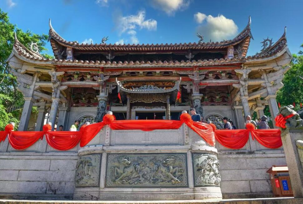 Ornate Chinese temple with carved stone railing, red fabric decor, and visitors on a sunny day.Meizhou Island Mazu Temple,Putian,Fujian,Chinatravel