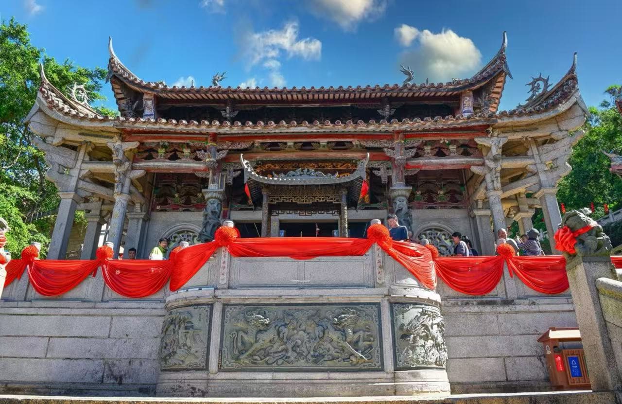 Ornate Chinese temple with carved stone railing, red fabric decor, and visitors on a sunny day.Meizhou Island Mazu Temple,Putian,Fujian,Chinatravel
