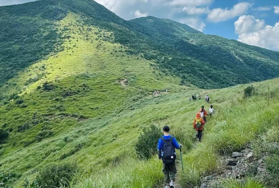 Mount Daiyun Scenic Area,Zhangzhou,Chinatour Hikers walking along a grassy mountain trail with blue sky and green hills in the background.