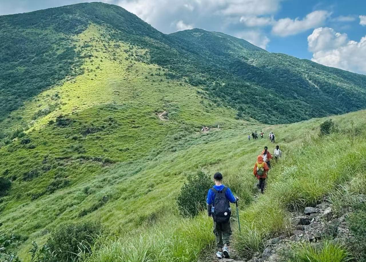 Mount Daiyun Scenic Area,Zhangzhou,Chinatour Hikers walking along a grassy mountain trail with blue sky and green hills in the background.