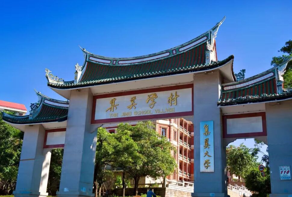 Jimei Educational Village,Xiamen,Chinatour Stone arch gate with traditional Chinese curved roofs, gold sign reading 'The Jimei School Village' and campus buildings visible behind under a clear blue sky.