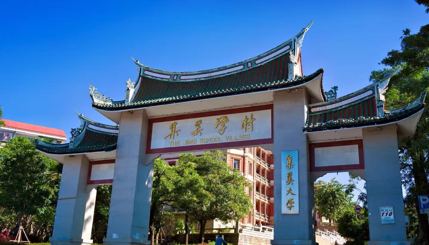 Jimei Educational Village,Xiamen,Chinatour Stone arch gate with traditional Chinese curved roofs, gold sign reading 'The Jimei School Village' and campus buildings visible behind under a clear blue sky.