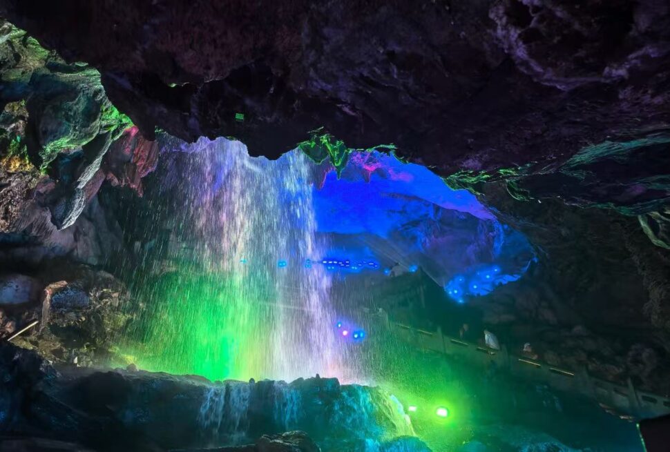 Shuanglong Cave ,Jinhua,Chinatour Cave interior with a colorful light show—green, blue, and purple glow on rocks and a waterfall mist.