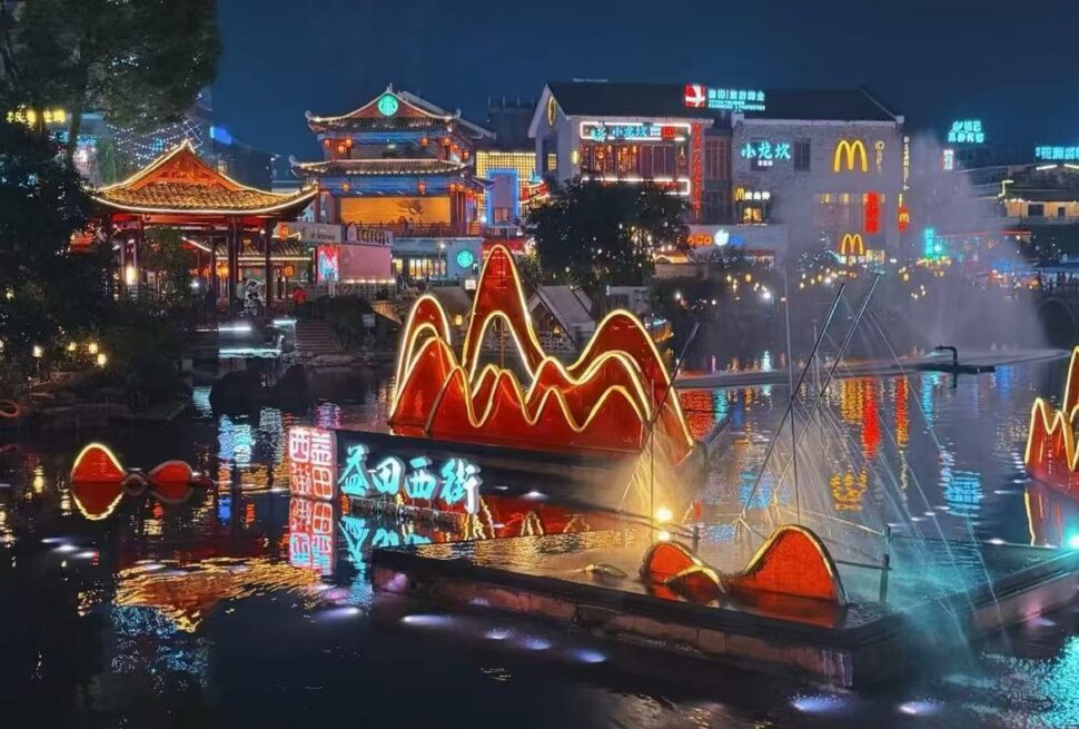 Nighttime river scene with glowing red neon mountain sculptures on the water and traditional Chinese architecture in the background.Yangshuo West Street,Yangshuo,Guangxi,Chinatravel