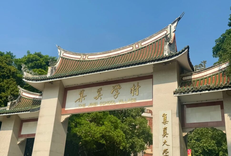 Jimei Educational Village,Xiamen,Chinatravel Entrance gate with traditional curved roof and gold inscription reading 'THE JIMEI SCHOOL VILLAGE' against a blue sky and green trees behind.