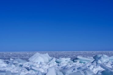 Ice-covered shore with jagged white ice chunks under a clear blue sky, Arctic horizon in the distance.Qinghai Lake,Xining,Qinghai