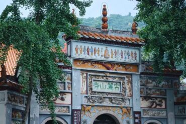 Ornate temple gate with gray stone walls, colorful murals of Buddhist figures, and trees framing the scene.Lushan Templen,Changsha,Hunan ,Chinatravel