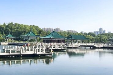 Green-roofed pavilions on a calm lake, connected by white bridges, with trees and a distant city skyline.East Lake Scenic Area,Wuhan,Hubei ,Chinatravel