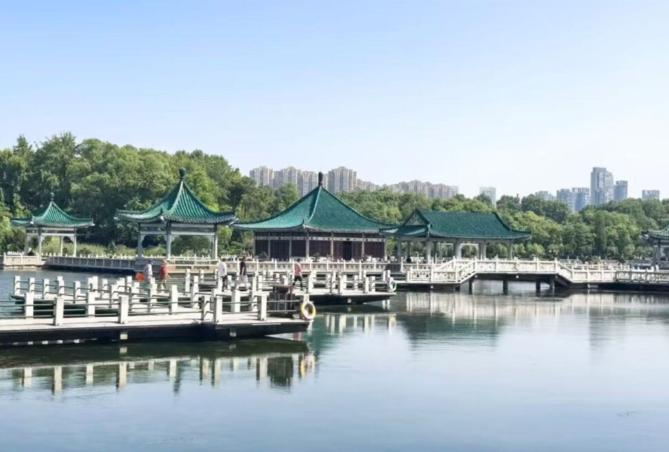 Green-roofed pavilions on a calm lake, connected by white bridges, with trees and a distant city skyline.East Lake Scenic Area,Wuhan,Hubei ,Chinatravel