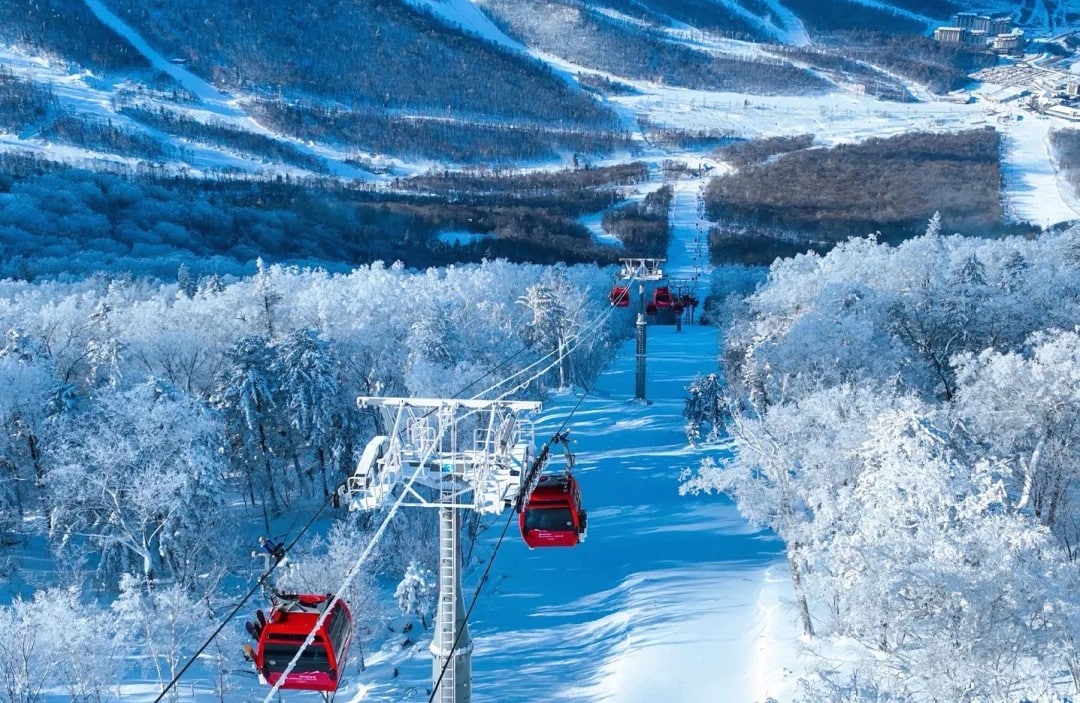 Snow-covered mountains and a ski lift with red gondolas gliding above a snow-blanketed forest.Jilin Beidahu Ski Resort,Chinatravel