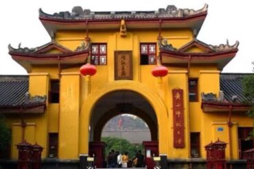 Yellow Chinese-style gate with curved roofs, red lanterns, and a central arch leading to a courtyard; people enter the site.Jingjiang Princes’ City,Guilin,Guangxi ,Chinatravel