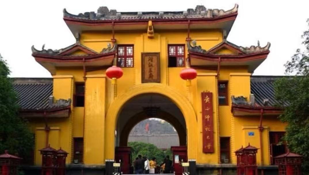 Yellow Chinese-style gate with curved roofs, red lanterns, and a central arch leading to a courtyard; people enter the site.Jingjiang Princes’ City,Guilin,Guangxi ,Chinatravel