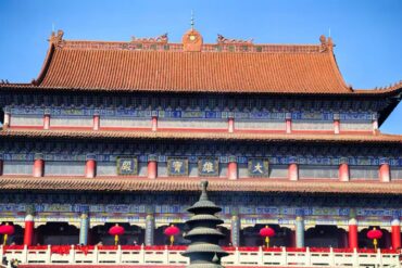 Front view of a traditional Chinese temple with blue and gold detailing, red columns, and a tiered roof under a clear blue sky, with red lanterns along the walkway.Kaifu Temple,Changsha,Hunan ,Chinatravel