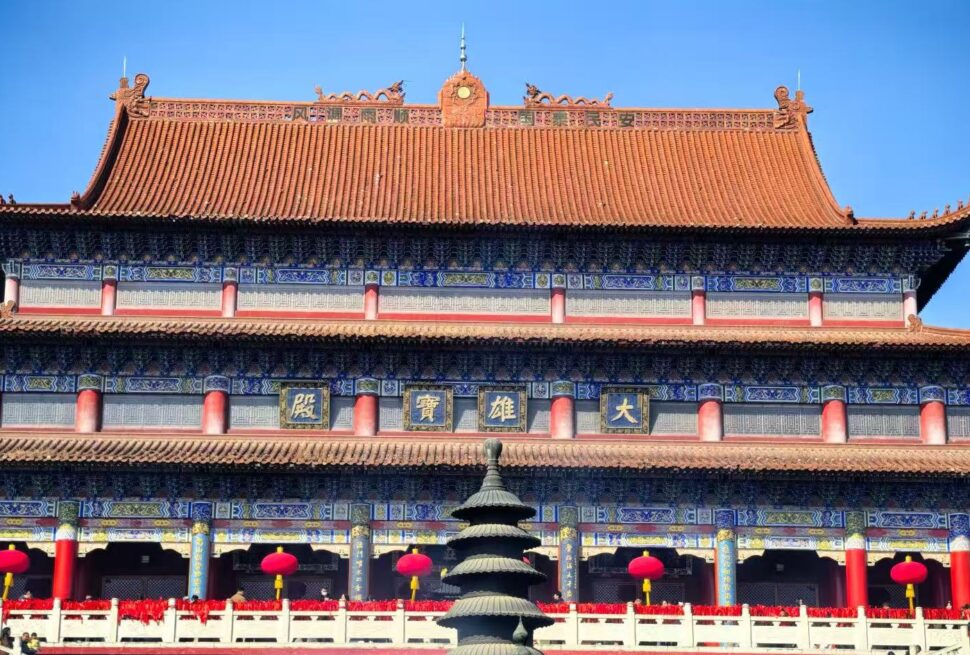 Front view of a traditional Chinese temple with blue and gold detailing, red columns, and a tiered roof under a clear blue sky, with red lanterns along the walkway.Kaifu Temple,Changsha,Hunan ,Chinatravel
