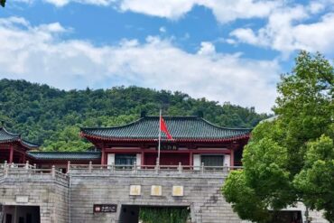 Traditional Chinese temple complex on a stone gate with red walls and a dark tiled roof, flagpole with a red flag against green hills and blue sky.Yuelu Mountain Park,Changsha,Hunan ,Chinatravel