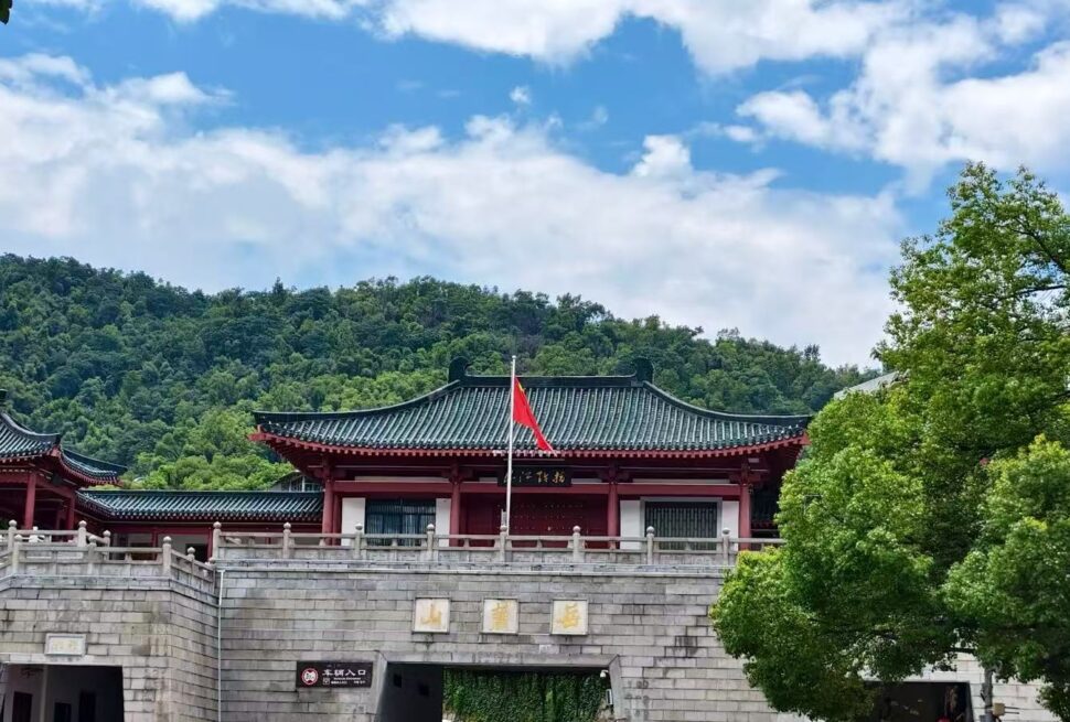Traditional Chinese temple complex on a stone gate with red walls and a dark tiled roof, flagpole with a red flag against green hills and blue sky.Yuelu Mountain Park,Changsha,Hunan ,Chinatravel