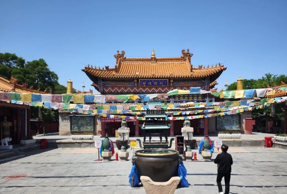 Traditional Chinese temple courtyard with a pagoda-style roof, colorful prayer flags, and a large bronze incense burner in the foreground.Dazhao Temple,Hohhot,Inner Mongolia
