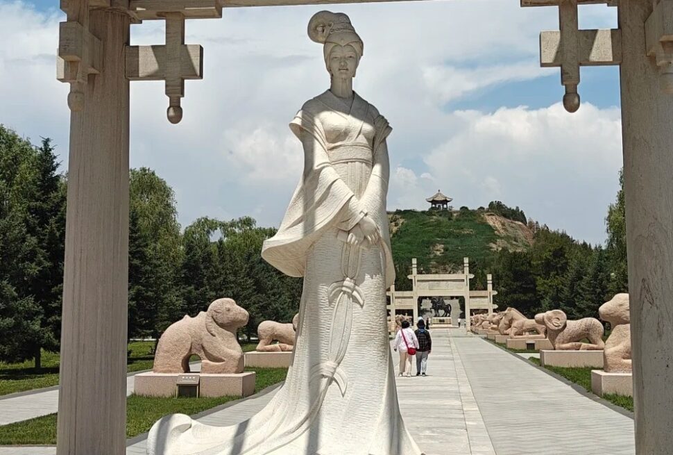 Large white statue of a woman in flowing traditional dress standing along a stone walkway, with stone animal sculptures lining the path and a hilltop pavilion in the distance.Zhaojun Tomb,Hohhot,Inner Mongolia,Chinatravel