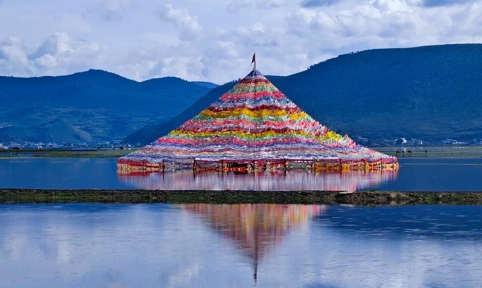 Colorful pyramid of prayer flags floating on a calm lake with mountain hills in the background, reflecting in the water,Napahai Lake,Shangri-La,Yunnan,Chinatravel