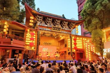 Outdoor Chinese cultural stage under a ornate temple gate with red lanterns, large audience watching a performance at dusk/evening.Huangxing Road Pedestrian Street,Changsha,Hunan ,Chinatravel