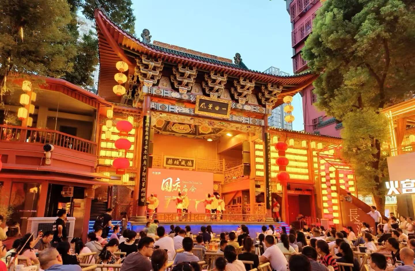 Outdoor Chinese cultural stage under a ornate temple gate with red lanterns, large audience watching a performance at dusk/evening.Huangxing Road Pedestrian Street,Changsha,Hunan ,Chinatravel