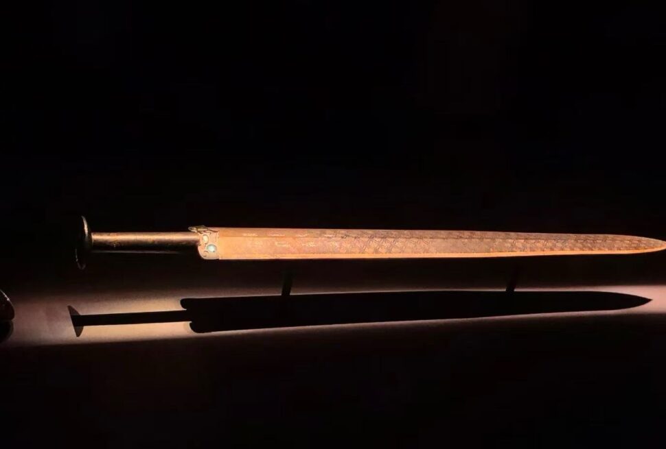 Ornate dagger with a metal hilt and long slim blade, placed above a brown sheath on a dark surface.Hubei Provincial Museum,Wuhan,Hubei ,Chinatravel