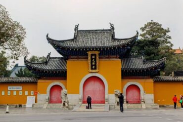 Temple gate with yellow walls and red arched doors, ornate black-tiled roof, stone lions guarding the entrance.Guiyuan Buddhist Temple,Wuhan,Hubei ,Chinatravel