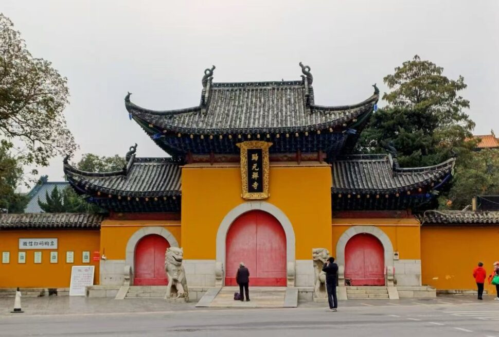 Temple gate with yellow walls and red arched doors, ornate black-tiled roof, stone lions guarding the entrance.Guiyuan Buddhist Temple,Wuhan,Hubei ,Chinatravel