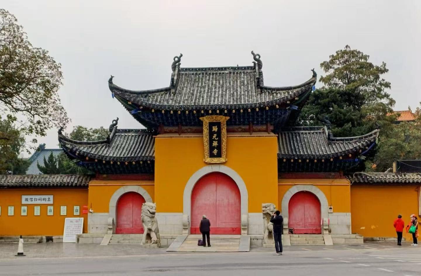 Temple gate with yellow walls and red arched doors, ornate black-tiled roof, stone lions guarding the entrance.Guiyuan Buddhist Temple,Wuhan,Hubei ,Chinatravel