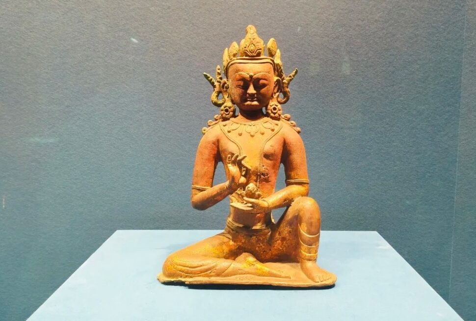 Terracotta statue of a seated deity on a blue pedestal, hands in a mudra gesture, against a blue wall.Hohhot Inner Mongolia Museum,Hohhot,Inner Mongolia,Chinatravel