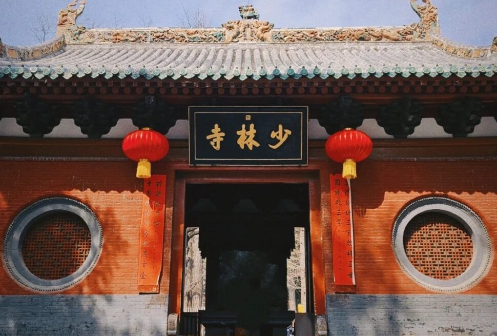 Entrance to a Shaolin Temple with red brick walls, round lattice windows, red lanterns, and a black plaque with gold Chinese characters.Shaolin Temple,Shaolin & Songshan Area,Henan,Chinatravel