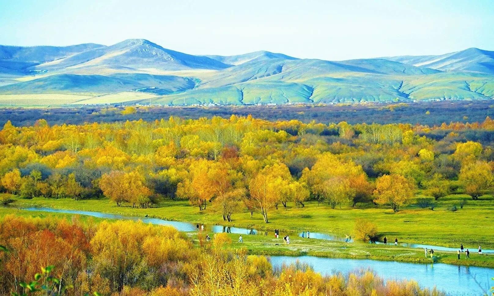 Hulunbuir Ergun Wetland,Hulunbuir,Chinatour Fall landscape with yellow and orange trees along a winding river, rolling fields and distant blue mountains.