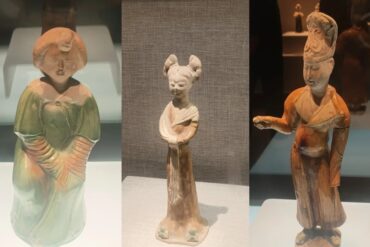 Henan Museum,Luoyang,Chinatour Triptych of ceramic figurines on display: a left green-gowned figure, a middle slim figure with two buns, and a right orange-robed figure with a raised arm.