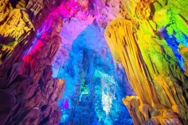 Cave interior lit with vibrant rainbow colors, showing stalactites and stalagmites along rocky walls.Reed Flute Cave,Guilin,Guangxi ,Chinatravel