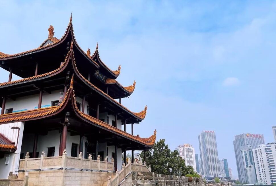 Traditional multi-story Chinese temple with ornate orange-tiled roofs in the foreground and modern high-rise buildings in the background under a blue sky.Tianxin Pavilion,Changsha,Hunan ,Chinatravel
